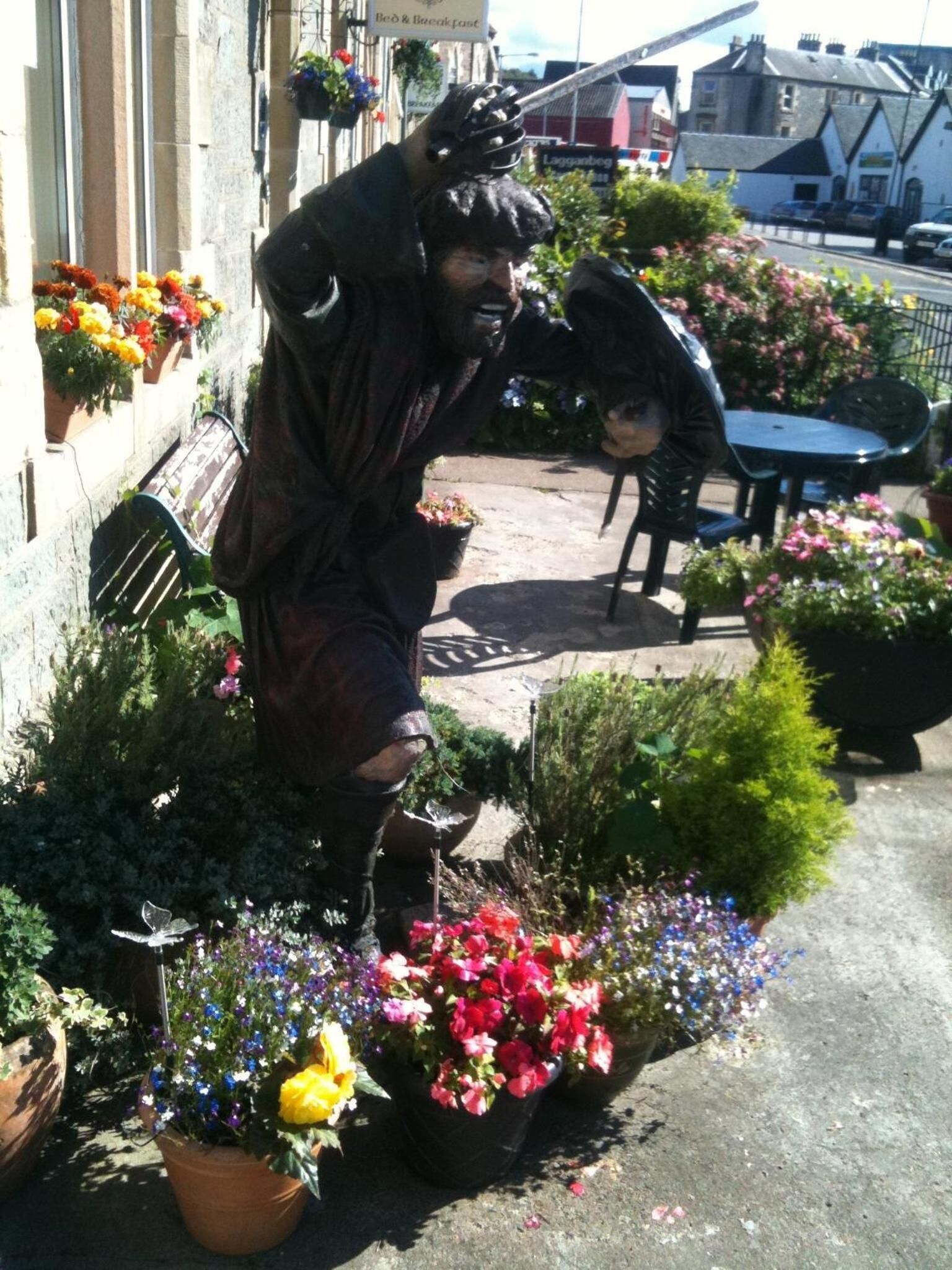 A statue of a person in a garden setting with potted plants and outdoor furniture.