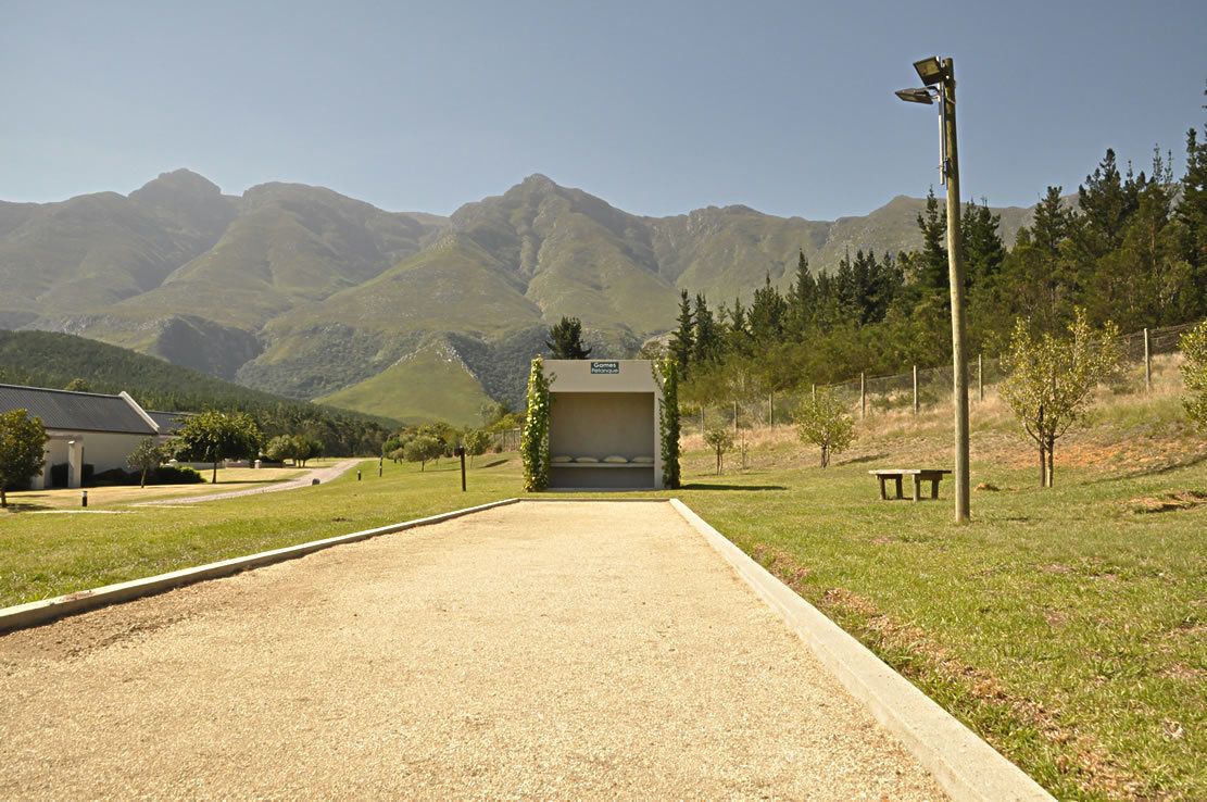 Un chemin de gravier mène à un bâtiment sur lequel est apposée une enseigne, le tout étant entouré de montagnes et de verdure.