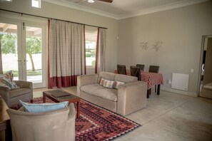 A living room with a beige sofa, a coffee table, and a dining area with a table and chairs. - Gaikou Lodge (Swellendam)