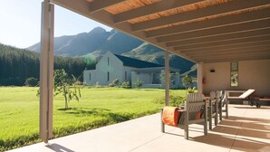 A covered outdoor area with a view of a white building and mountains in the background. - Gaikou Lodge (Swellendam)