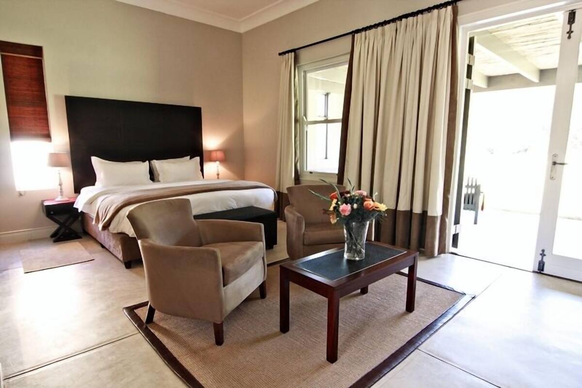 A hotel room with a bed, two armchairs, a coffee table, and a vase of flowers.