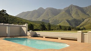 A swimming pool with a mountain backdrop, surrounded by a white building with a flat roof. - Gaikou Lodge (Swellendam)