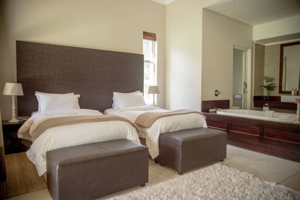 A bedroom with two beds, a large mirror, and a bathroom with a bathtub.