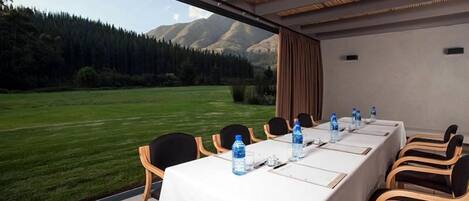 A conference room with a table set for a meeting, chairs, and a view of a mountainous landscape.