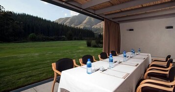 Un salón de conferencias con una mesa lista para una reunión, sillas y vistas a un paisaje montañoso.