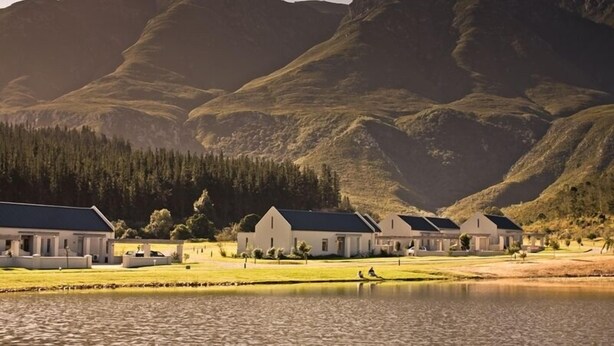 A resort with multiple white buildings, a lake, and mountains in the background. - Gaikou Lodge (Swellendam)
