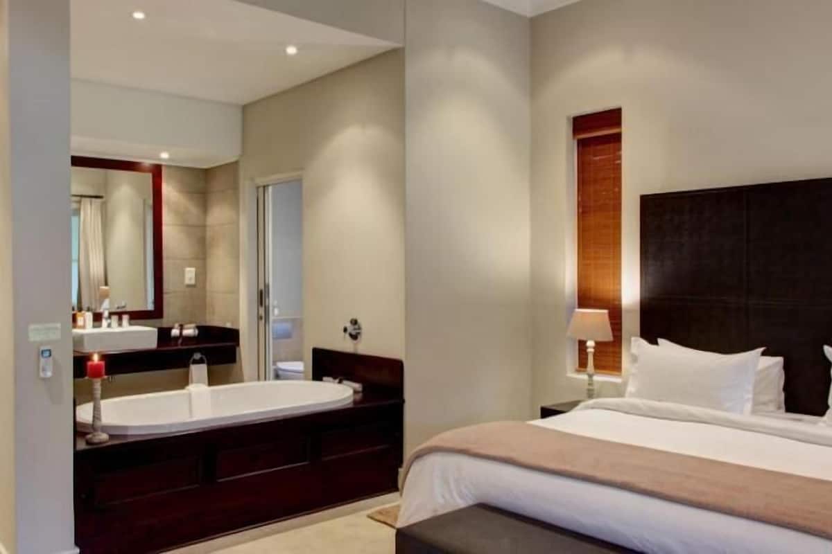 A modern hotel room with a large bed, a double vanity with a mirror, and a separate shower area.