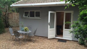 Una casita con un patio, una mesa con sillas y una planta en maceta.