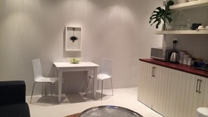 Una cocina moderna con armarios blancos, microondas y cafetera en la encimera. Hay un comedor con una mesa blanca y dos sillas.