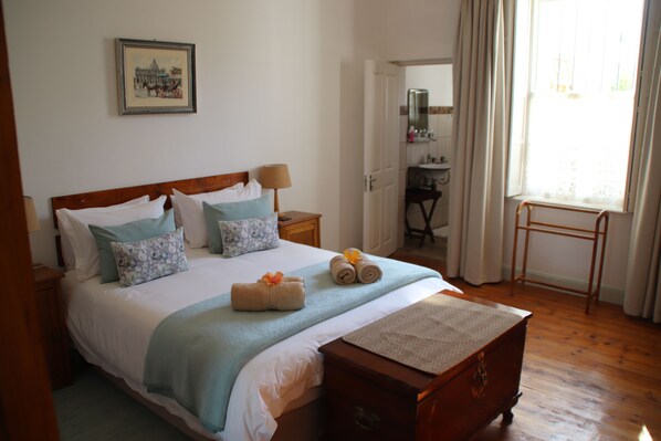 A neatly made bed with a headboard, a bedside table with a lamp, a wooden bench, and a window with curtains.