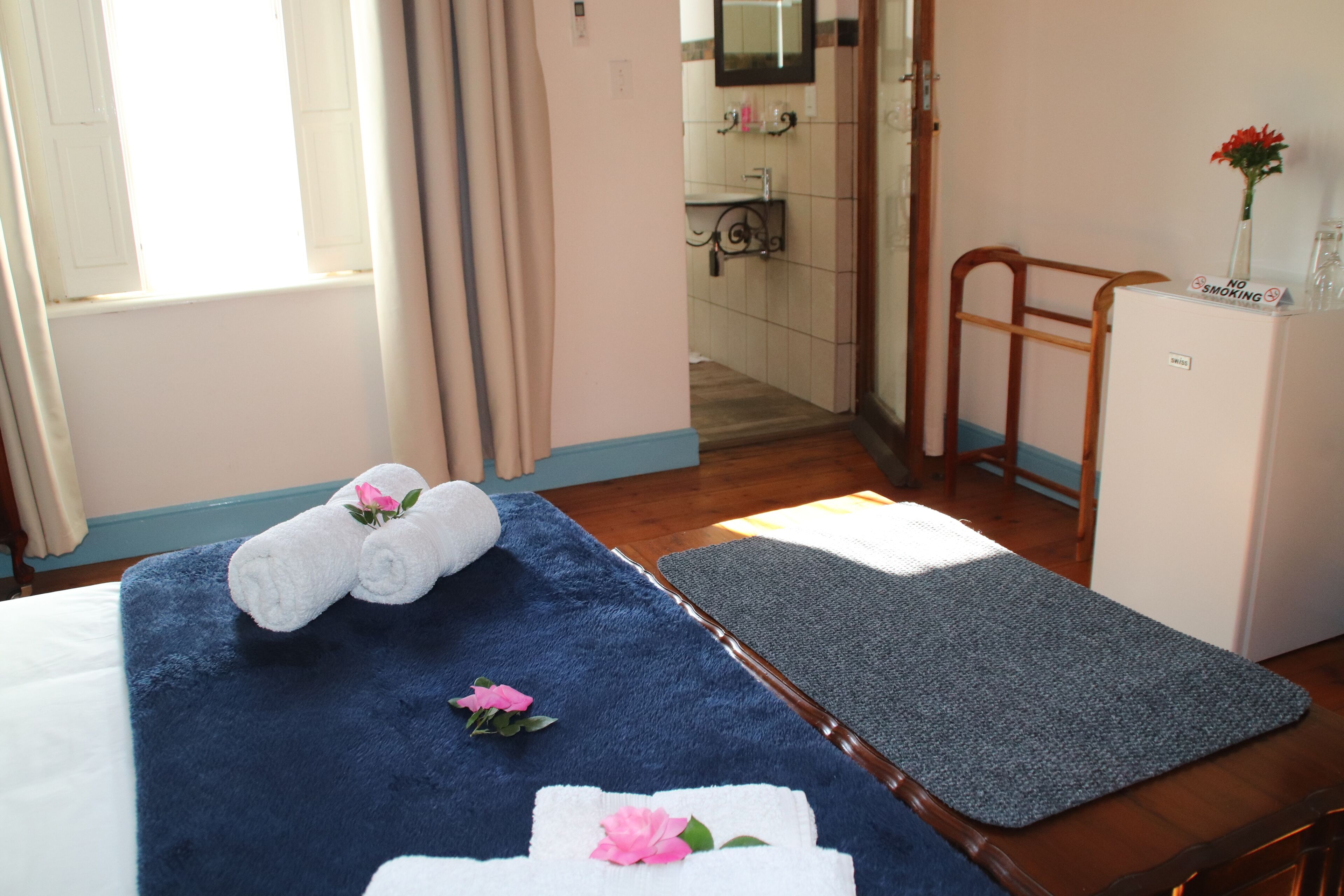 Quarto de hotel com uma cama, um tapete de banho azul, uma cadeira de madeira e um frigorífico.