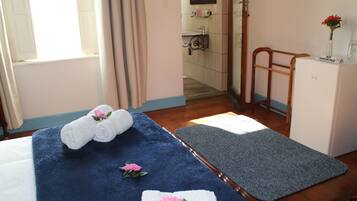 Quarto de hotel com uma cama, um tapete de banho azul, uma cadeira de madeira e um frigorífico.