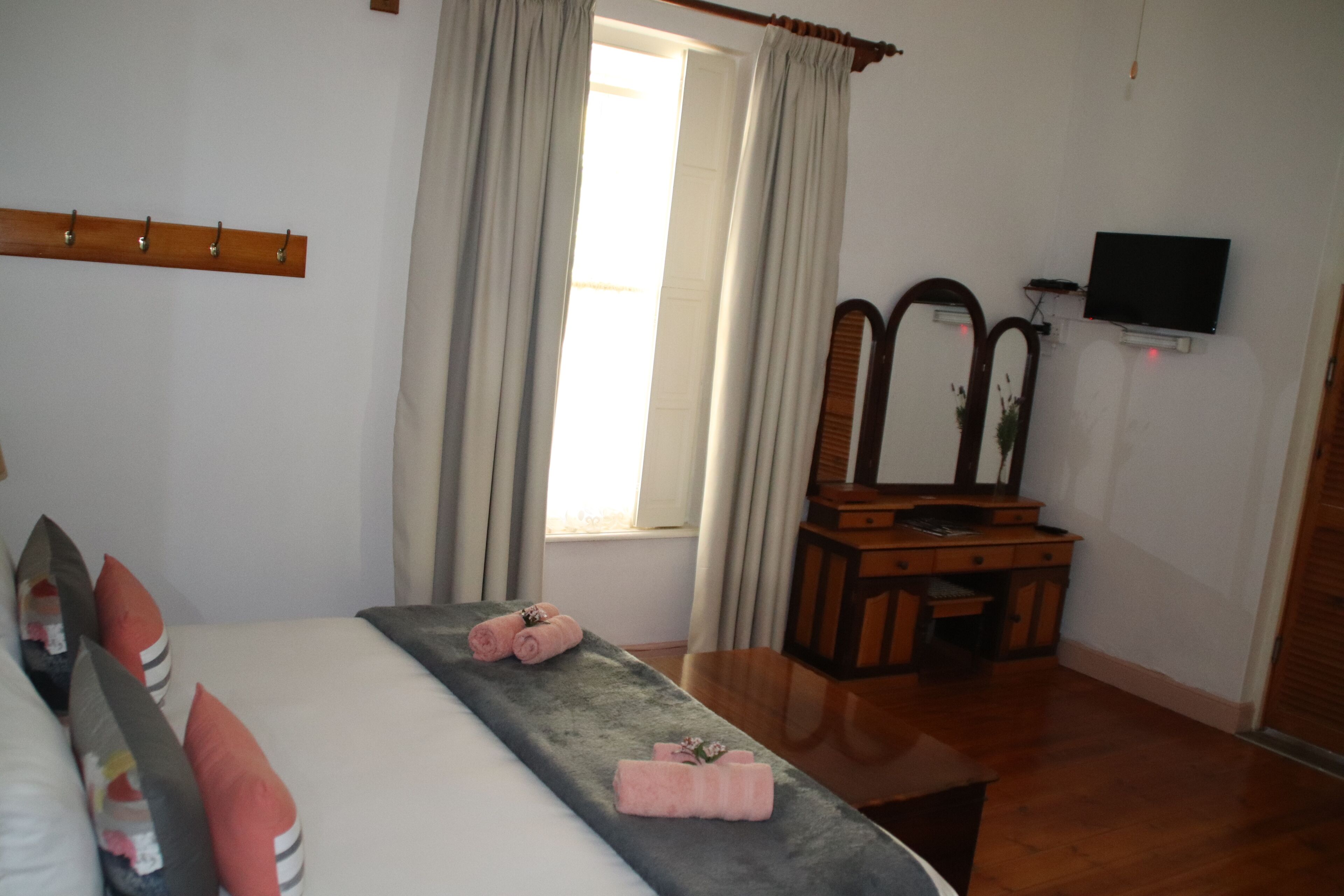 A hotel room with a bed, a wooden dresser, a television, and a window with curtains.
