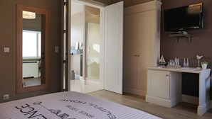 A bedroom with a bed, a wardrobe, a television, and a desk with a mirror.