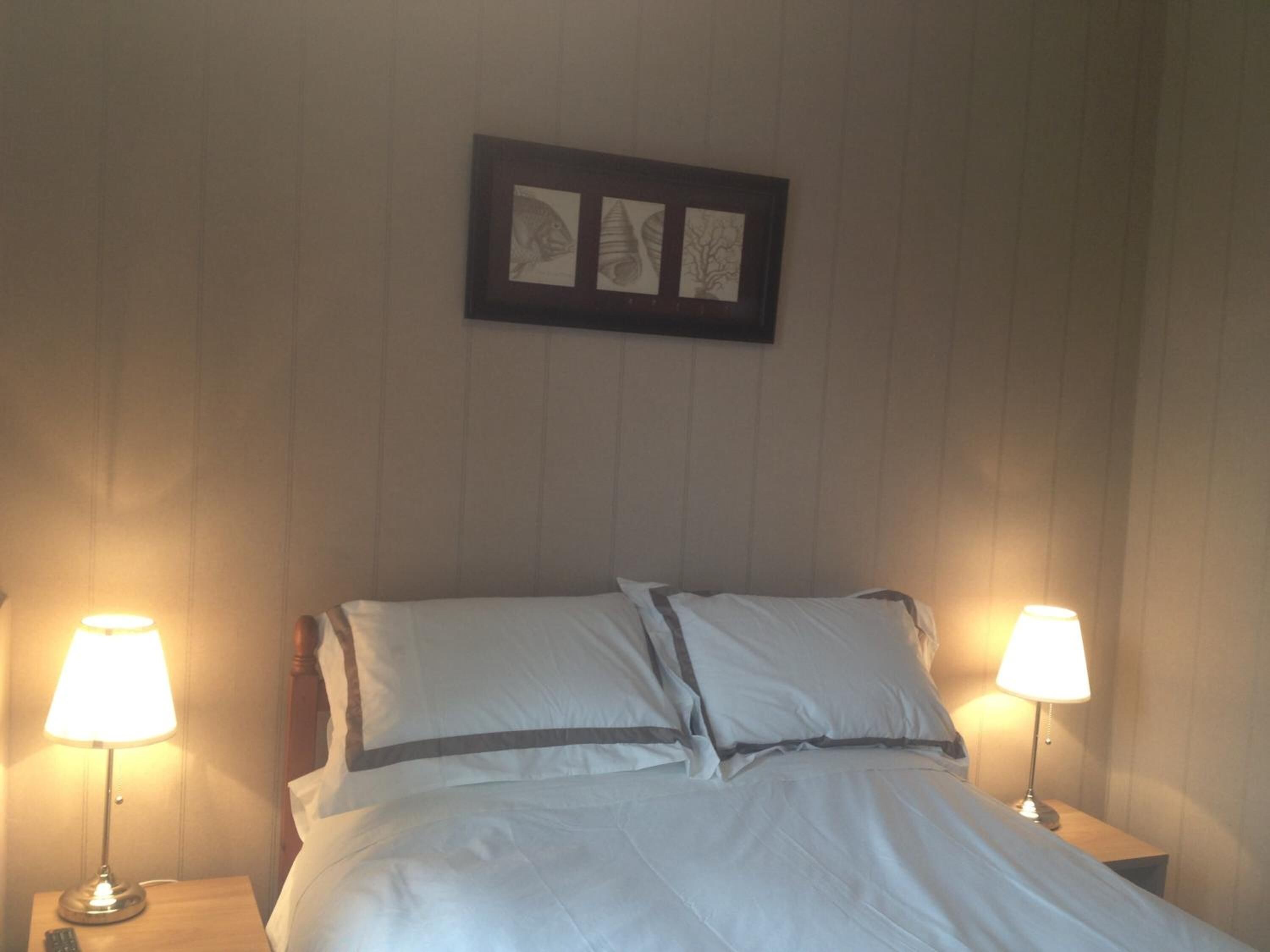 A neatly made bed with white linens and a gray accent, flanked by two bedside lamps on wooden nightstands.