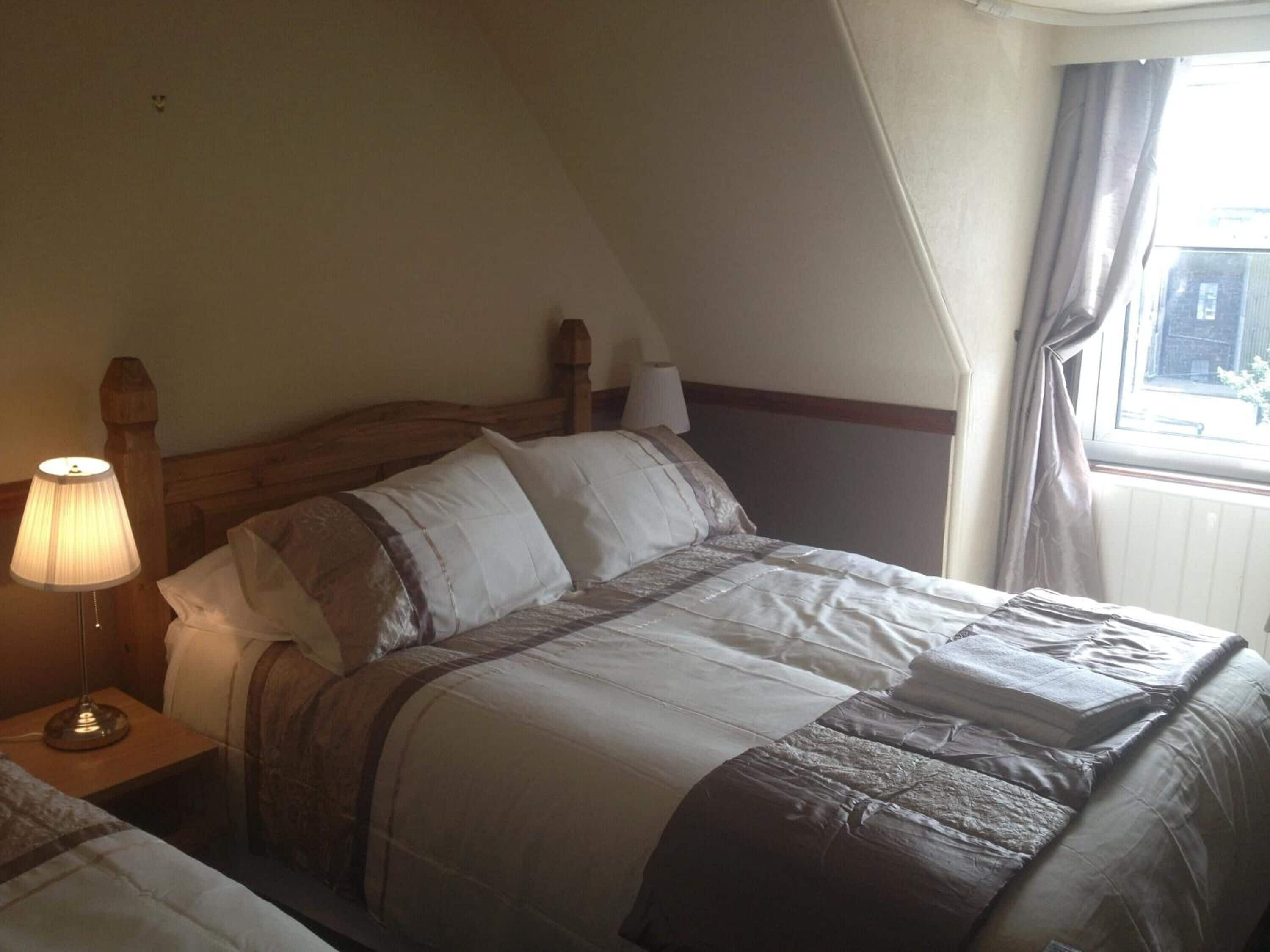 A bedroom with a wooden headboard, a bedside lamp, and a window with curtains.
