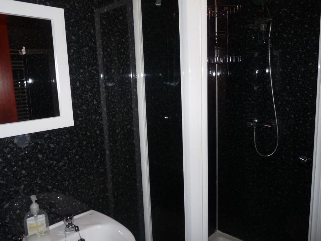 Un baño con lavabo de mármol negro, un espejo y cabina de ducha.
