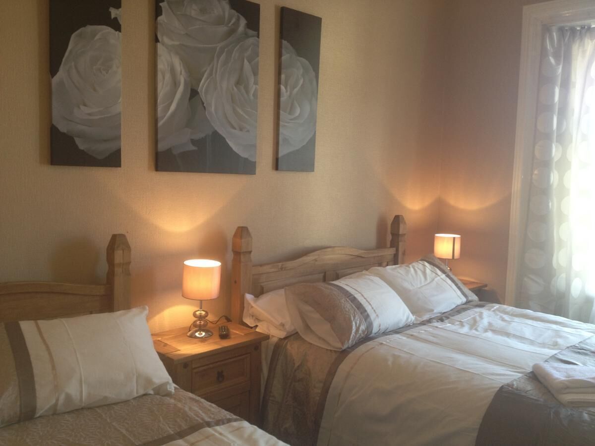 A hotel room with two beds, a wooden headboard, bedside lamps, and a window with curtains.