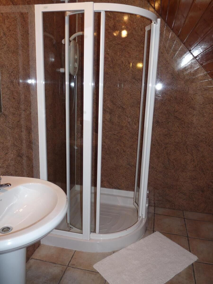 A bathroom with a glass-enclosed shower, a sink, and a small rug on the floor.