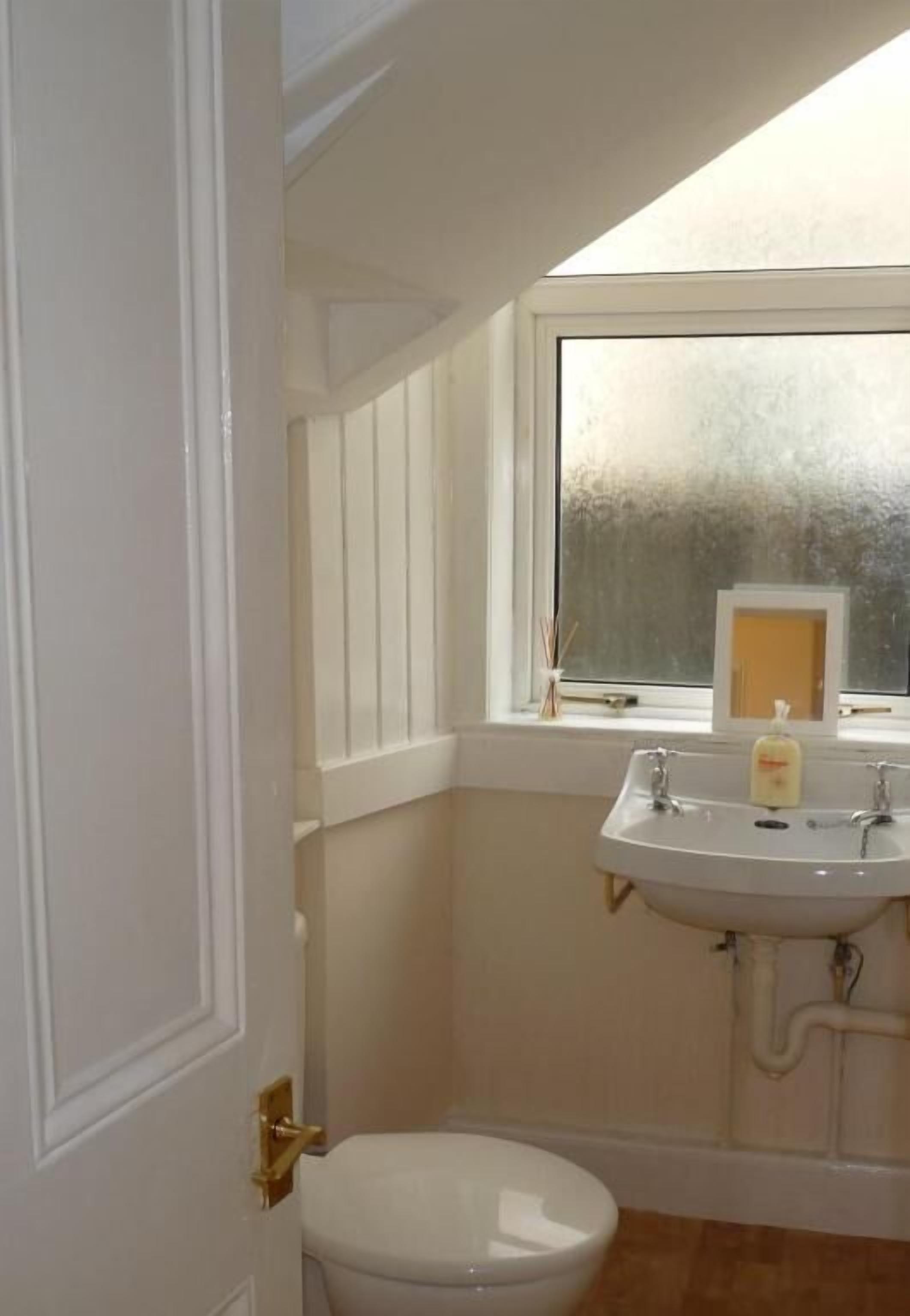 Une salle de bain avec un lavabo blanc, des toilettes et une fenêtre.