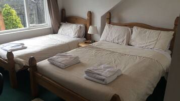 Quarto com duas camas de solteiro, uma mesa de cabeceira com abajur e uma janela com cortinas.