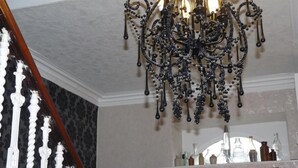 Un candelabro con múltiples brazos y detalles colgantes, una escalera de madera con barandillas blancas y una puerta con marco y paneles de vidrio.