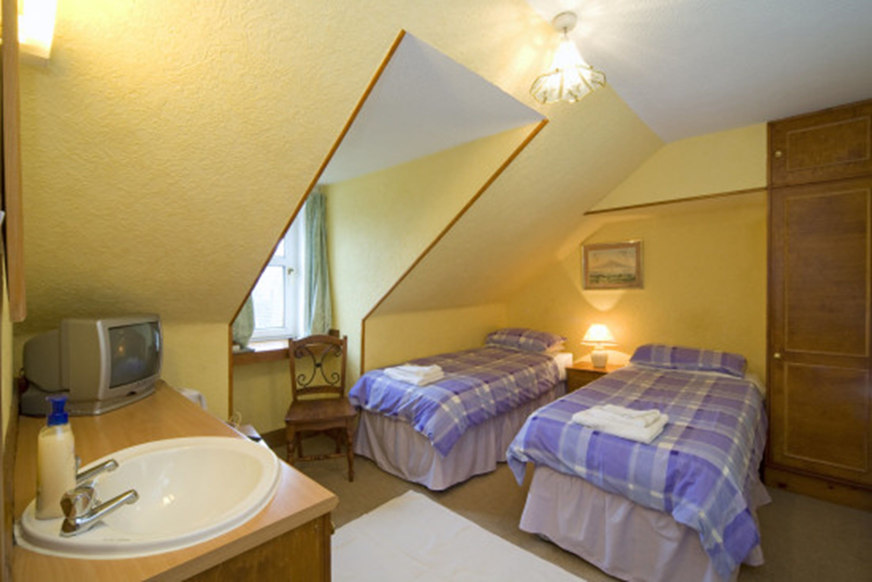Ein kleines, gemütliches Schlafzimmer mit zwei Betten, einem Sessel, einem Schreibtisch mit Computer und einem großen Spiegel.