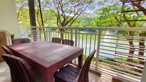 A covered outdoor dining area with a table and chairs, overlooking a body of water and greenery. - Dr Calayan's 2BR Condo at Pico De Loro (Nasugbu)