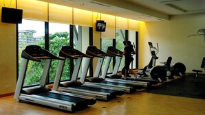 A gym with treadmills lined up against a wall with large windows, a television mounted on the wall, and exercise equipment on the floor. - Dr Calayan's 2BR Condo at Pico De Loro (Nasugbu)