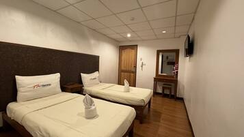 A hotel room with two beds, a wooden headboard, a small desk, a mirror, and a TV on the wall.