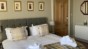 A neatly made bed with white linens and a plaid throw blanket, a wooden door, and framed pictures on the wall. - Thornsgill House B&B (Leyburn)