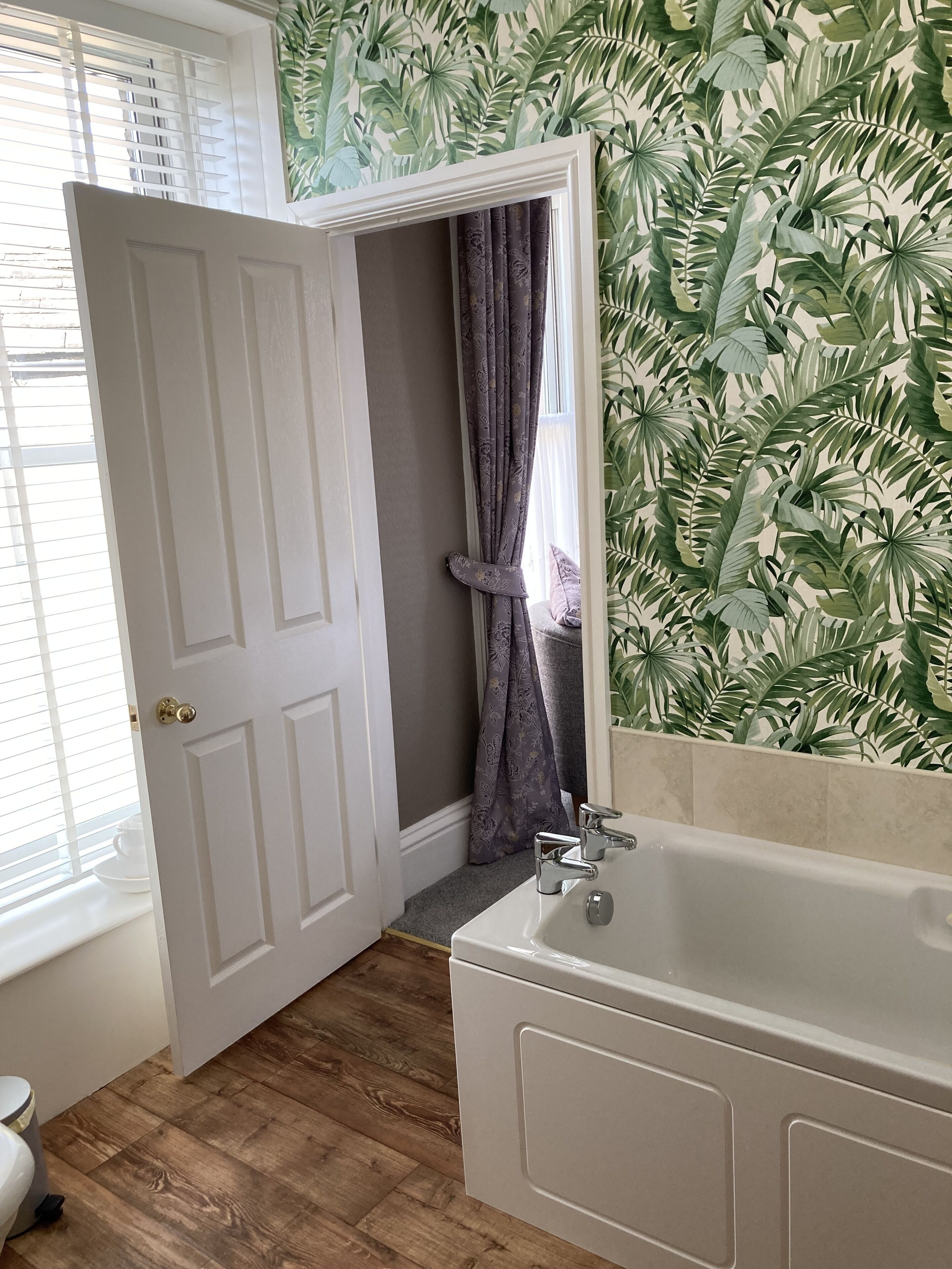 Un baño con una bañera, una puerta que da a otra habitación y una ventana con persianas.