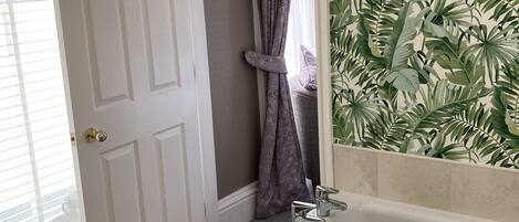Un baño con una bañera, una puerta que da a otra habitación y una ventana con persianas.
