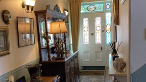 A hallway with a wooden table, chairs, a lamp, and a decorative mirror. There is a door with stained glass windows and a patterned floor. - Thornsgill House B&B (Leyburn)