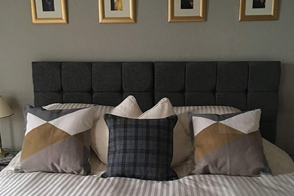 Cama com cabeceira escura, roupa de cama listrada e várias almofadas em diferentes padrões e cores.