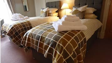 Ett hotellrum med två sängar, var och en med ett rutigt sängöverkast och kuddar. Det står en lampa på nattduksbordet bredvid en av sängarna.