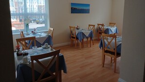 A dining area with tables set for four, wooden chairs, and a view of the street through a large window. - Palm Court (Weymouth)