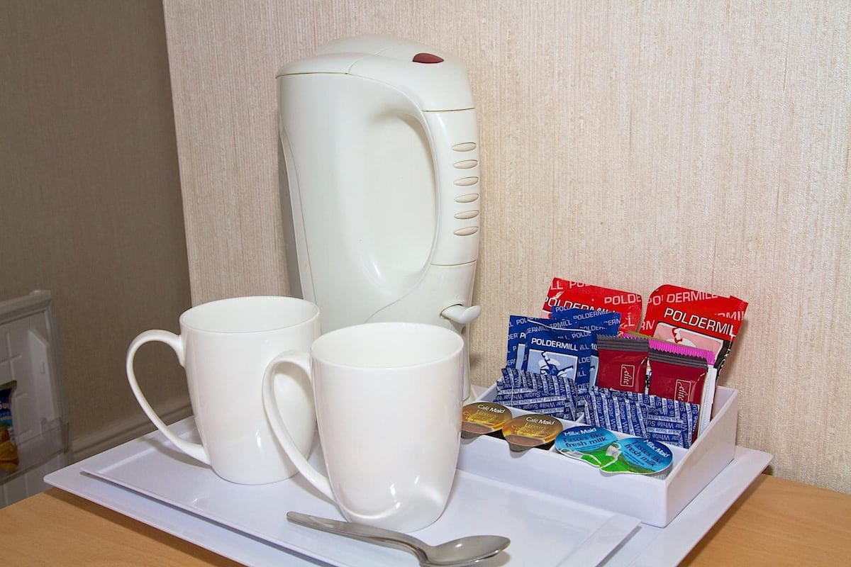 A white electric kettle, two white mugs, a spoon, and a tray with tea bags.
