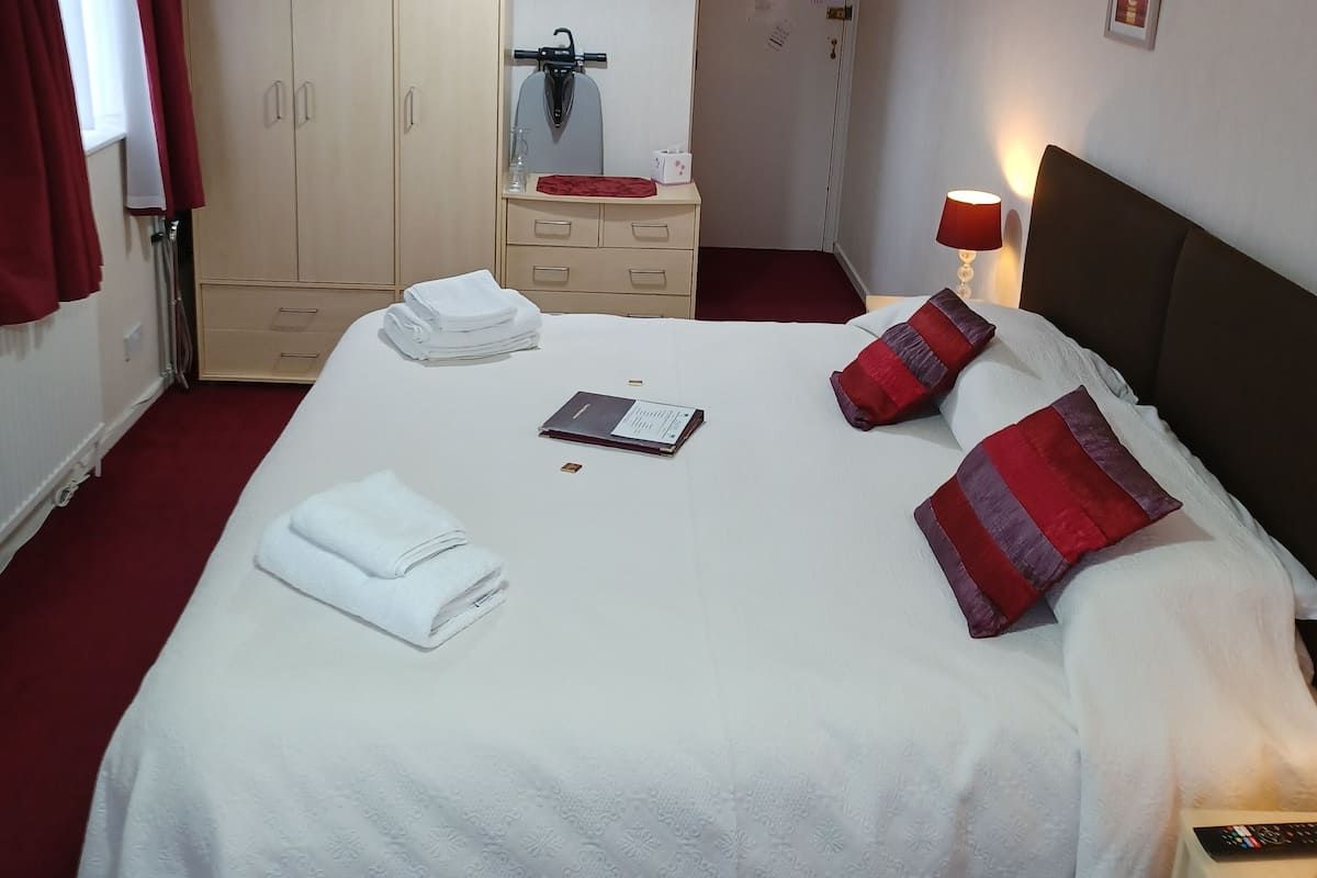 A hotel room with a large bed, a wardrobe, a desk, and a mirror.