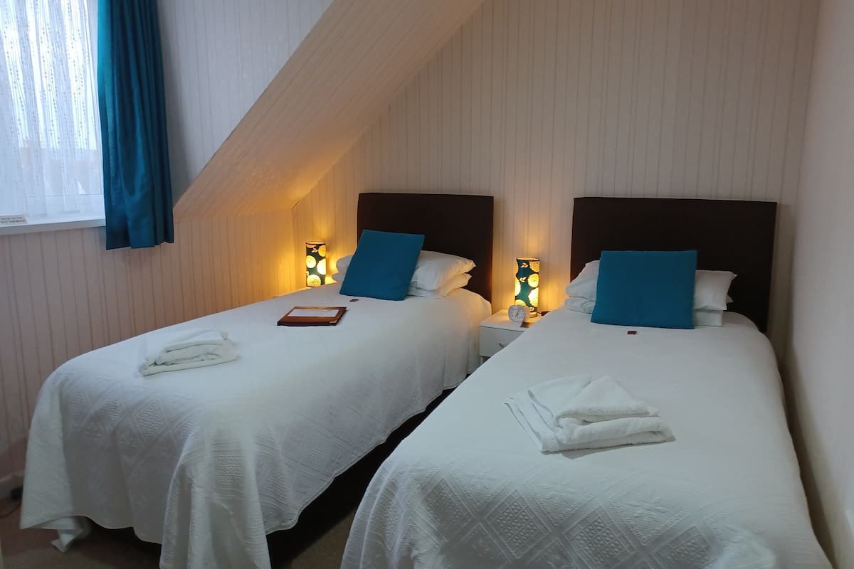 Two twin beds in a room with sloped ceilings, each with a nightstand, a lamp, and a folded towel.