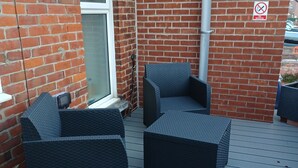 A patio with two dark wicker chairs and a small table, a brick wall, a window, and a 'no smoking' sign. - Palm Court (Weymouth)