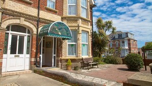 A corner building with a green awning, a bench, and a palm tree. - Palm Court (Weymouth)