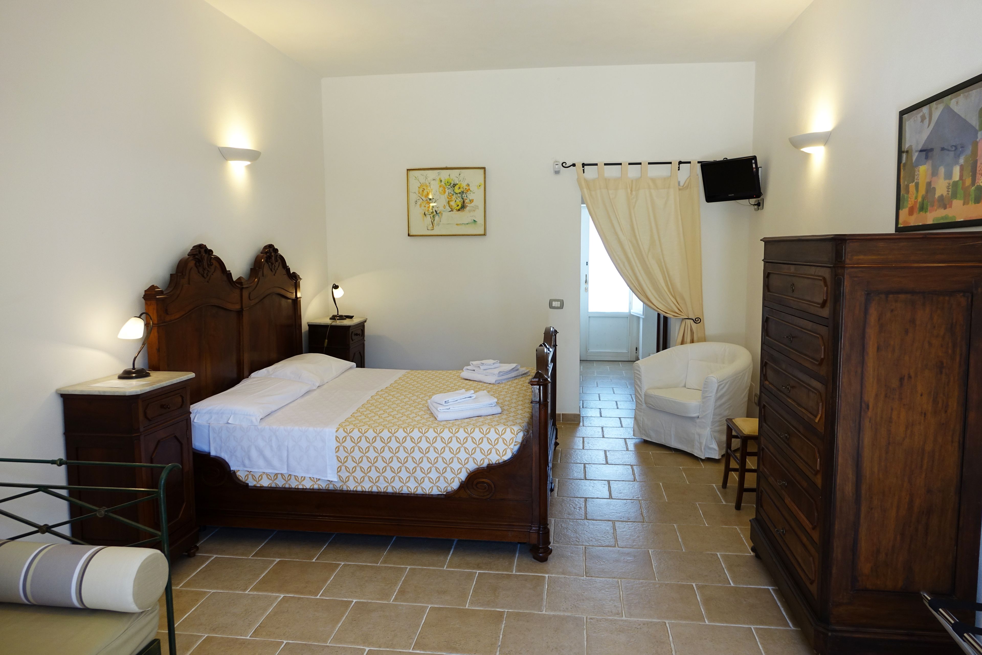 Quarto com cama de madeira, mesa de cabeceira, cômoda, cadeira e televisão na parede.