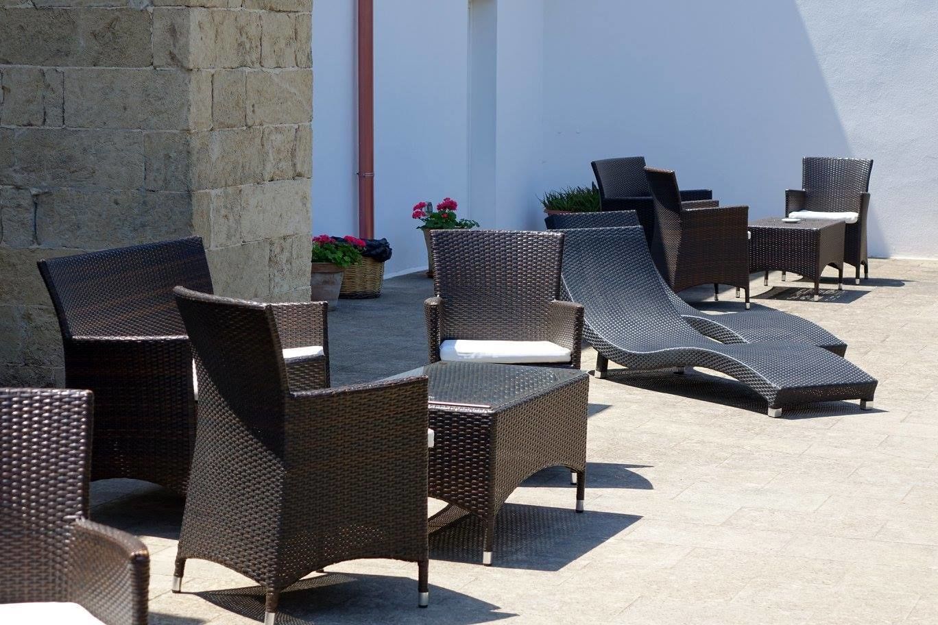 Terrassenmöbel aus Rattan draußen, mit einer Steinmauer und Blumentöpfen.