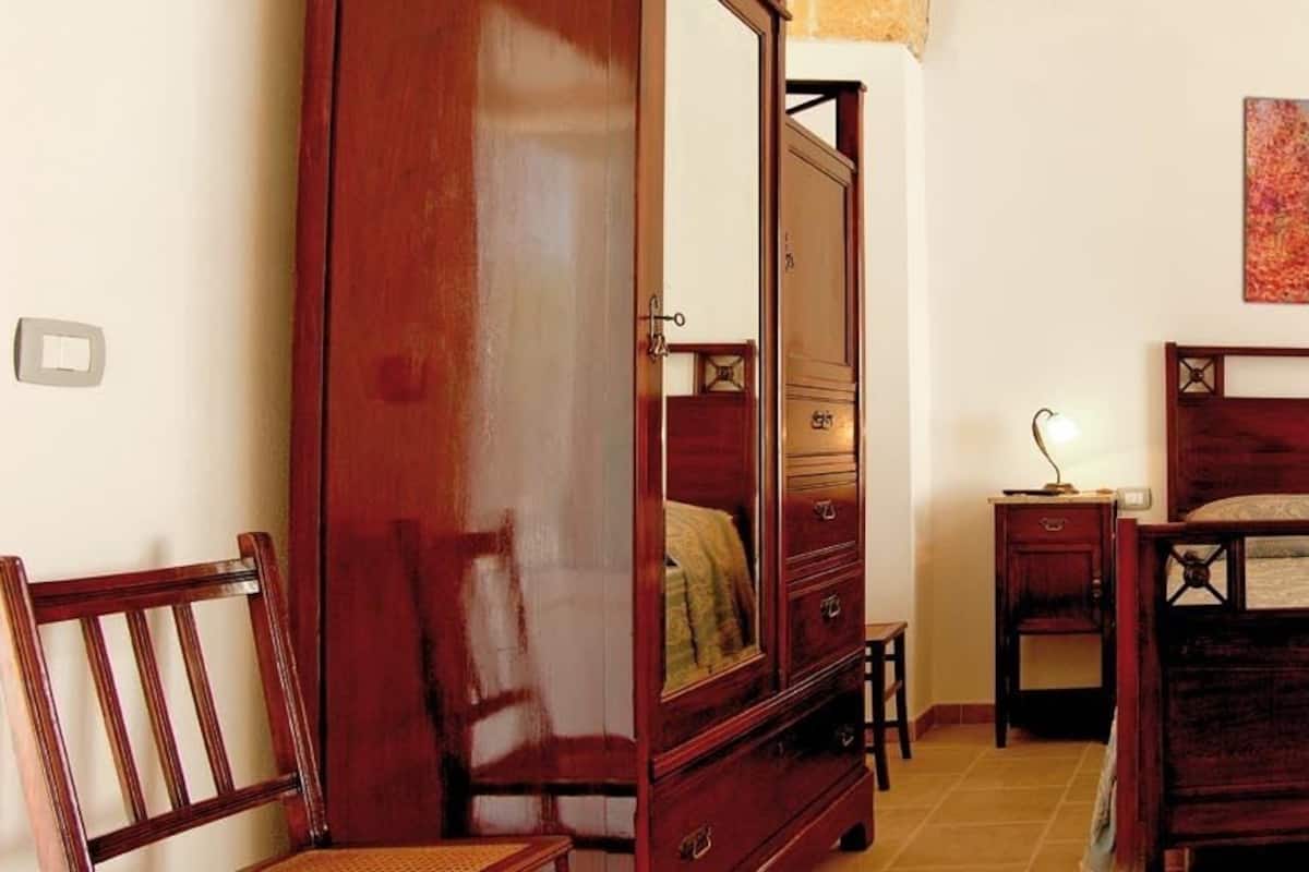 A bedroom with a wooden bed, a nightstand, a chair, a dresser, and a painting on the wall.