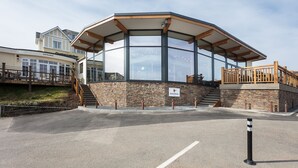 A modern building with a glass enclosure, wooden deck, and a stone facade. - Oystercatcher Apartments (Wadebridge)