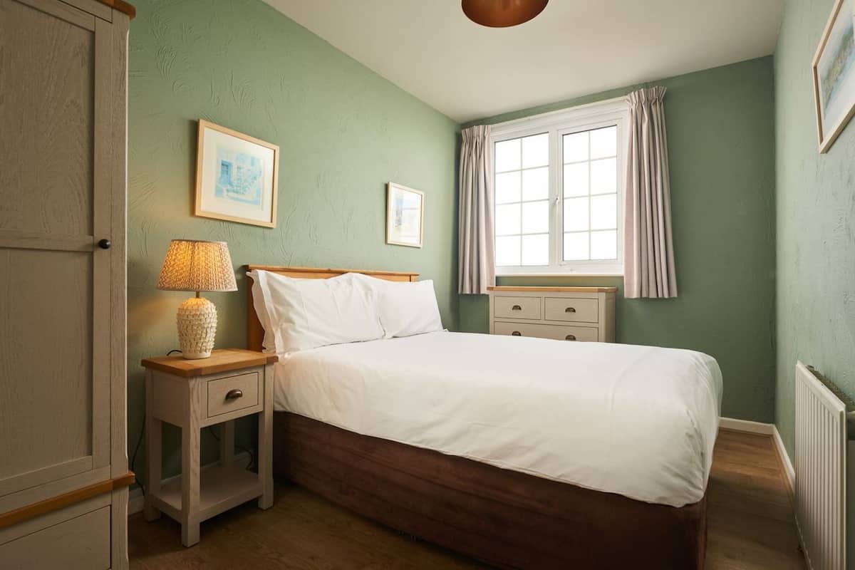 A bedroom with a bed, bedside table, lamp, and a window with curtains.