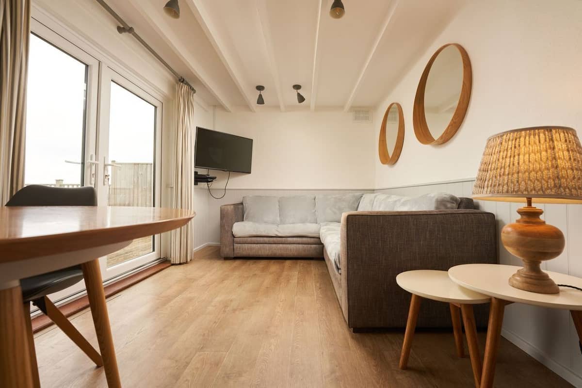 A modern living room with a sofa, a dining table, and a TV mounted on the wall.