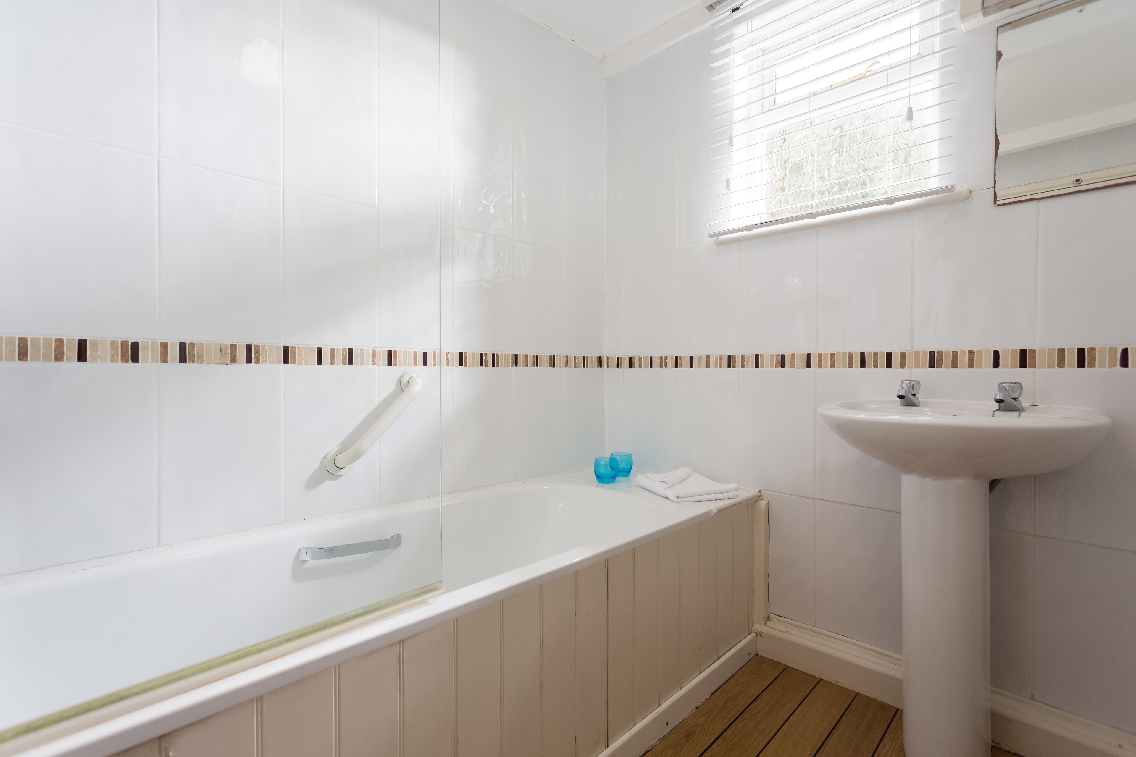 A bathroom with a white bathtub, a sink, and a window with blinds.