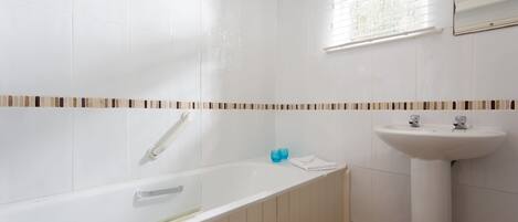 Un baño con una bañera blanca, un lavabo y una ventana con persianas.